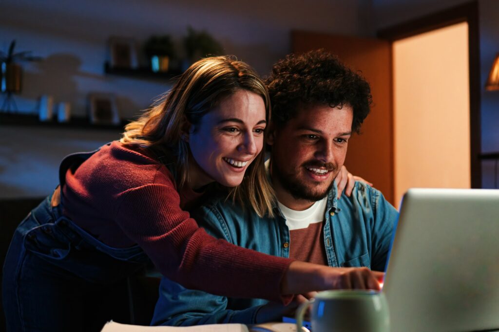 Young happy caucasian couple browsing on internet using a laptop to search sale at home. Excited