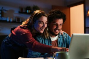 Young happy caucasian couple on internet using a laptop to perform due diligence to buy a home. Excited
